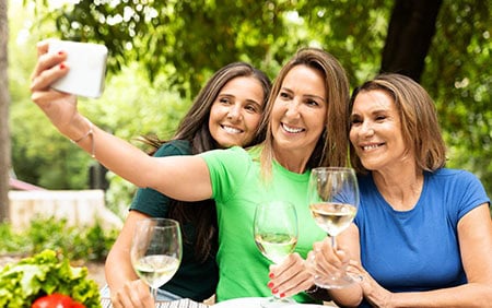 Three smiling middle aged women on hormone replacement therapy taking a selfie with wine outdoors