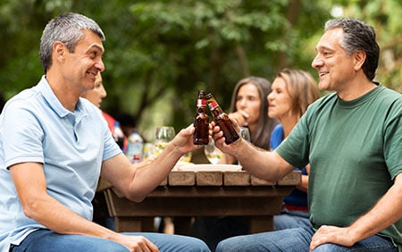 Two men happy with hormone replacement therapy toasting bottled beer at a picnic table outdoors