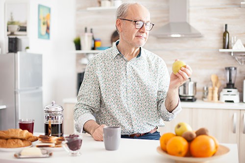 Older man looking at an apple in his hand while standing in his kitchen
