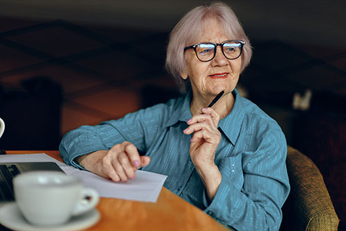 Older woman lost in thought with a pen to her chin at the kitchen table