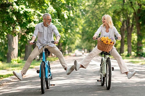 Smiling middle aged couple riding bicycles through the park