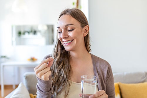 Smiling young woman preparing to take her thyroid medication with water sitting on her couch