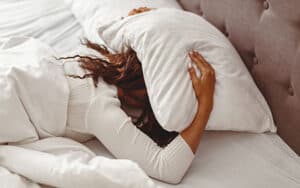 Woman in menopause suffering from insomnia holding her pillow over her head in bed
