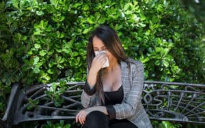 Young woman with poor immune system sneezing into a tissue on a park bench